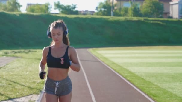 Vrouwelijke loper training in het stadion, het dragen van een koptelefoon. — Stockvideo