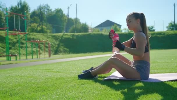 Втомлена дівчина п'є воду після тренування на стадіоні . — стокове відео