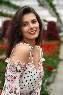 Gülümseyen genç kadın kırmızı çiçeklerin yanında poz veriyor.. 