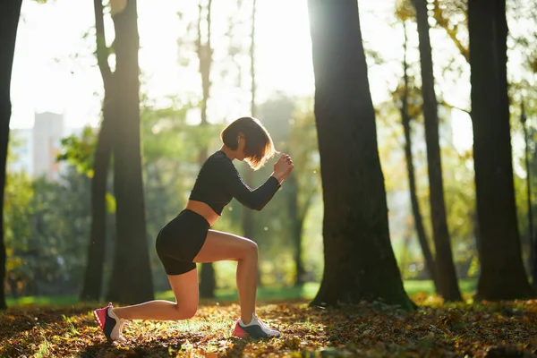 Urocza kobieta w stroju sportowym squatting w parku — Zdjęcie stockowe