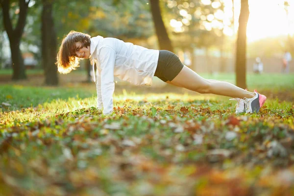 Silna młoda dama ćwiczy deskę w słonecznym parku — Zdjęcie stockowe
