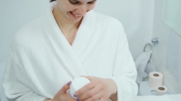 Charming woman in bathrobe using facial cream — Stock Video