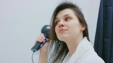 Çekici bir kadın banyoda saç kurutuyor.