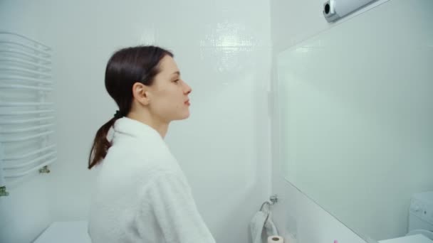 Kobieta bada się w lustrze w białej łazience. — Wideo stockowe