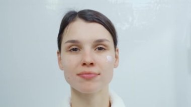 Kadın yüz bakımı yapıyor ve nemlendirici sürüyor..