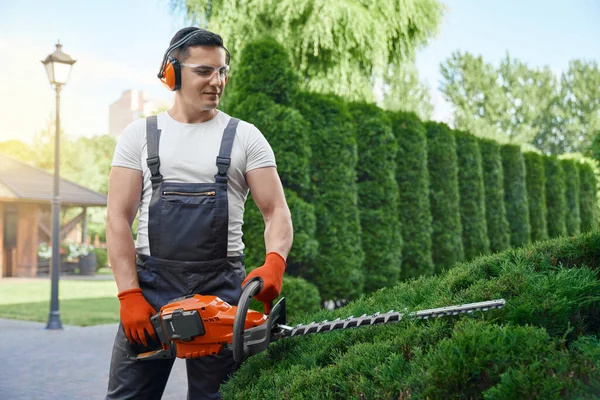 Hombre usando un recortador eléctrico para dar forma a los arbustos al aire libre — Foto de Stock
