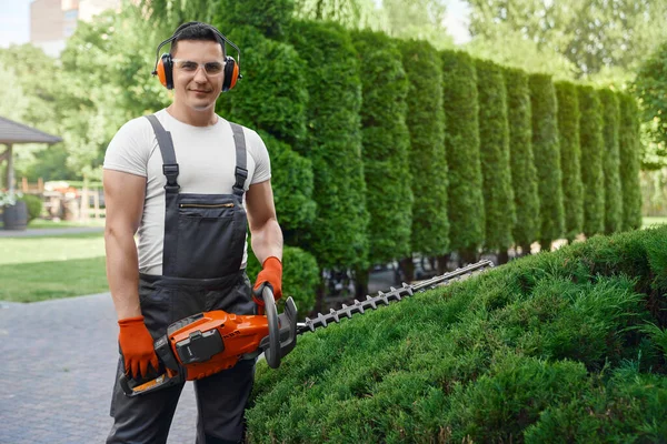 Mies poseeraa puutarhassa sähköinen trimmeri käsissä — kuvapankkivalokuva