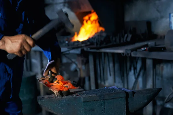 Людина в комбінезоні кування розплавленого металу на ковадлі — стокове фото