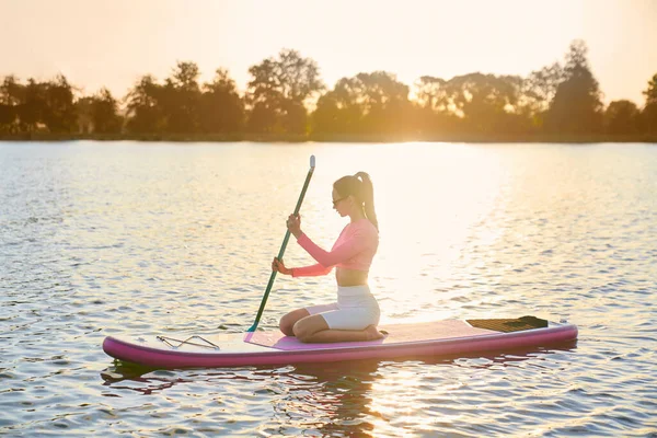 Kobieta pływająca samotnie na pokładzie supboard na jeziorze miasta — Zdjęcie stockowe