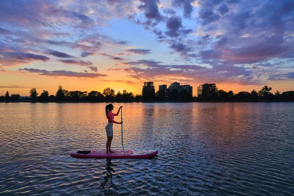 Mulher ativa nadando na prancha de jantar durante o pôr do sol no lago — Fotografia de Stock