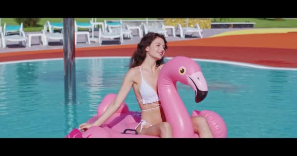 Lächelnde Frau im Bikini sitzt auf aufblasbarem Flamingo — Stockvideo