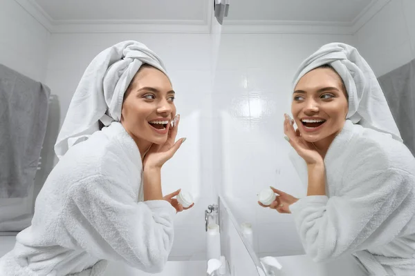 Mujer sonriente usando crema para la cara en el baño. —  Fotos de Stock