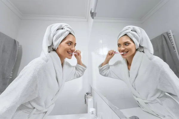 Mujer en bata blanca después de cepillarse los dientes de ducha en el baño. —  Fotos de Stock