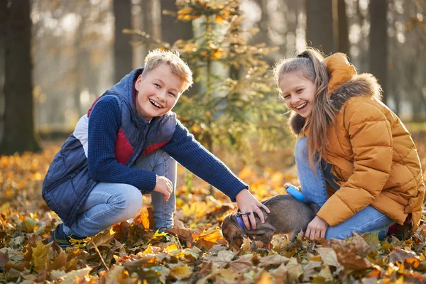 Junge und Mädchen lächeln und genießen gute Zeit mit Haustier im Park Herbst. — Stockfoto