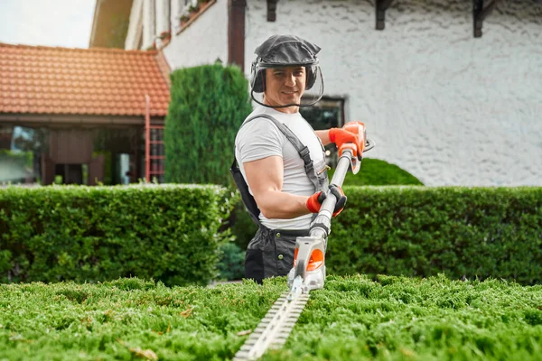 Tukang kebun menggunakan pemangkas pagar listrik untuk bekerja di luar ruangan — Stok Foto