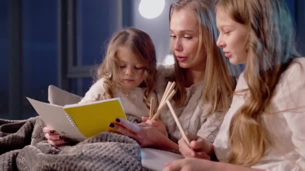 Duas meninas sentadas no sofá com a mãe e pintando no álbum — Vídeo de Stock