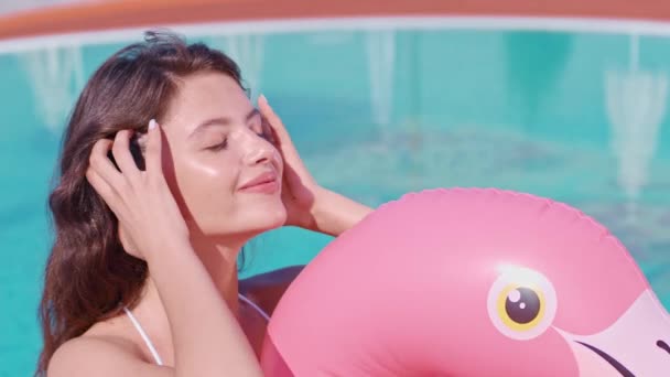 Positieve vrouw zwemmen op opblaasbare flamingo in zwembad — Stockvideo