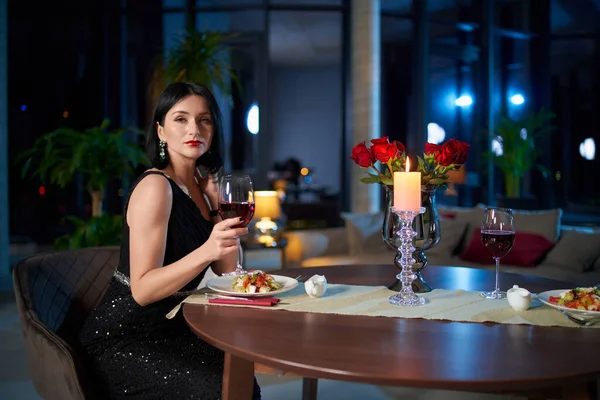 Frau in elegantem Kleid sitzt bei einem Glas Wein am Tisch — Stockfoto