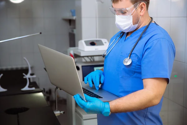 adult doctor in mask with laptop and medical tools in operating room at the hospital