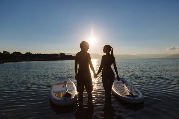 Silhouette di bella coppia con sup serf e pagaia al mare — Foto Stock