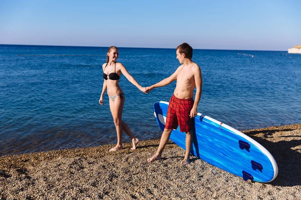 Pareja joven con sup board en la playa. Concepto de deporte, estilo de vida — Foto de Stock