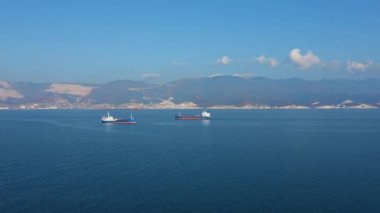 Güneşli bir günde deniz limanından ayrılan iki büyük kargo gemisinin hava aracı görüntüsü.