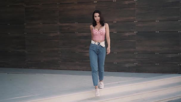 Женщина-модель в красном топе и джинсах идет вперед к камере — стоковое видео