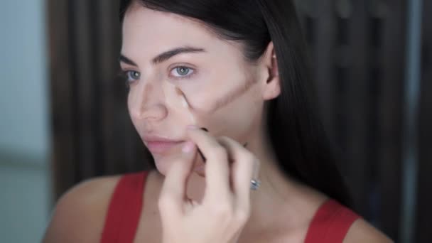 Make-up artiesten toe te passen highlighter op verhoogde gebieden van mooie jonge vrouwen gezicht — Stockvideo