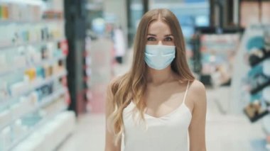 Koridorların arasında maske takmış beyaz bir kadın yürüyor. 
