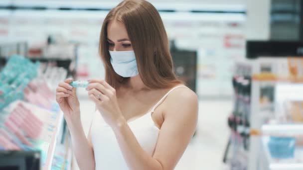 의료용 마스크를 쓴 젊은 코카서스 소녀가 마스카라를 시험하고 있습니다. 쇼핑 개념 — 비디오