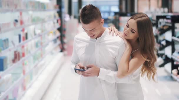 Charmant meisje vraagt haar vriendje chatten in smartphone om te gaan winkelen — Stockvideo