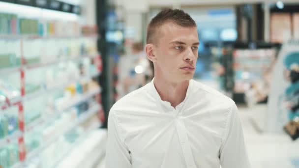 Handsome purposeful young guy in white shirt walks through the supermarket — Stock Video