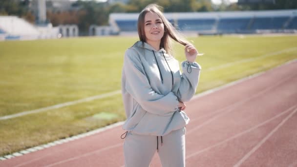 Pozitivní krásná kavkazská dívka pózující na stadionu v šedé teplákové soupravě — Stock video