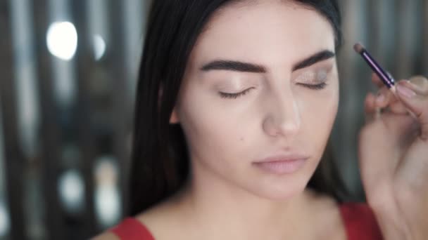 Maquiagem artista aplica sombra nos olhos de jovem morena caucasiana — Vídeo de Stock