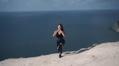 Ağır çekimde spor giyimli hoş bir kız elastik bantla çömeliyor. 