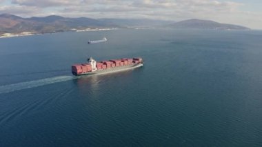 Dalgalarda yüzen büyük kırmızı kargo gemisinin havadan görüntüsü.