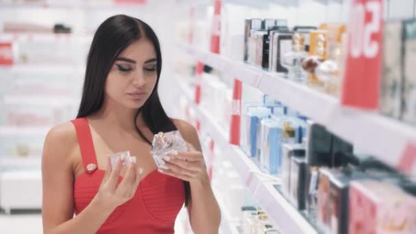 Jovem morena encantadora em um vestido vermelho escolhe um perfume — Vídeo de Stock