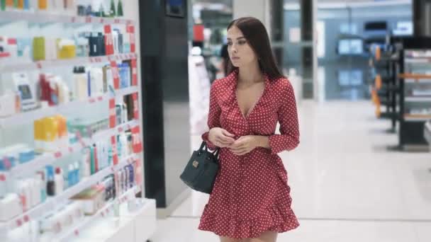 Sexy junge brünette Mädchen in rotem Kleid geht in Supermarkt einkaufen — Stockvideo