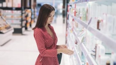 Kırmızı elbiseli zinde genç esmer kadın organik el kremini seçiyor. 