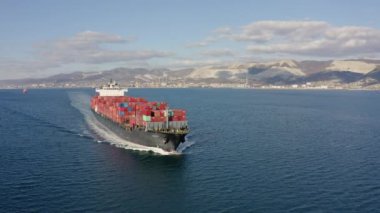 Deniz dalgaları üzerinde yüzen kırmızı konteynırlı büyük kargo gemisinin havadan görüntüsü. 