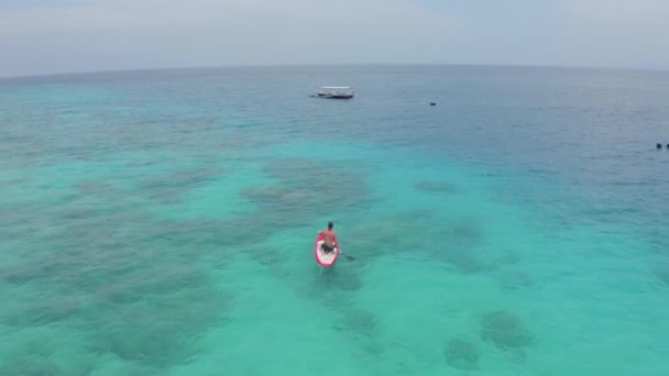 Vista aérea del joven turista flota en barco rojo en aguas azules claras — Vídeo de stock