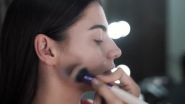 Makyaj sanatçısı beyaz kadına fırçayla toz uyguluyor.