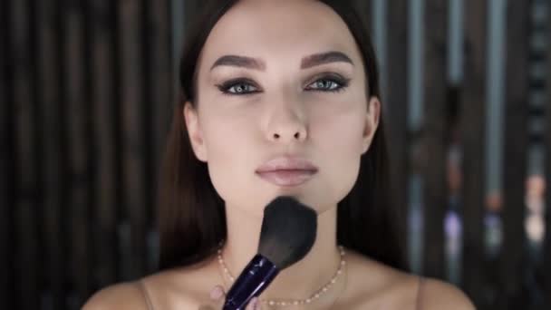 Hermosa mujer joven con maquillaje brillante aplicando polvo facial — Vídeo de stock