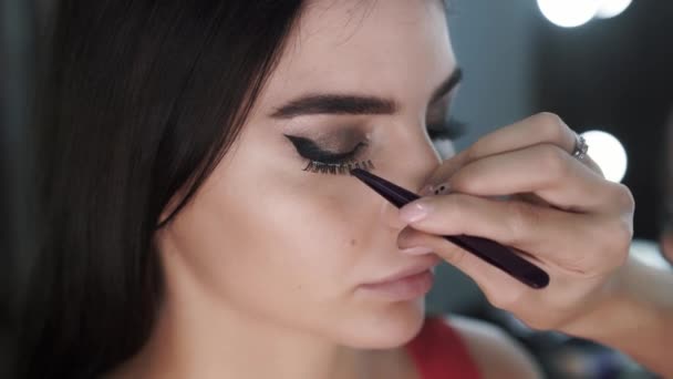 Close-up maquillaje artista palos pestañas falsas de un hermoso modo femenino joven — Vídeos de Stock