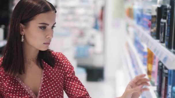 Söt ung brunett i en klänning med prickar välja kosmetiska produkter — Stockvideo