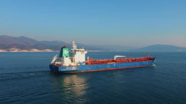 Güneşli bir günde deniz limanından ayrılan büyük kargo gemisinin hava görüntüsü.