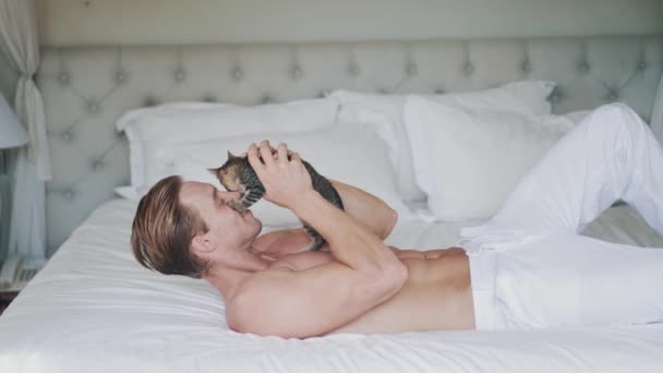 Deportivo caucásico hombre juega con bonito poco gatito en la cama — Vídeo de stock