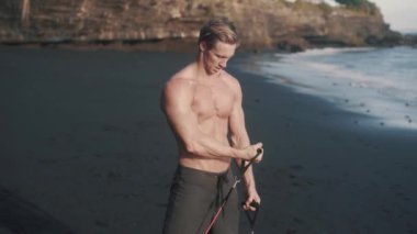 Genç atletik adam kumlu sahilde pazılarını ve trisepslerini çalıştırıyor..