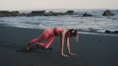 Genç beyaz kadın ıslak kumsalda bacak egzersizi yapıyor..