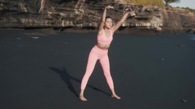 Spor giyimli genç beyaz bir kadın deniz kıyısında yarım yamalak yamaç yapıyor..